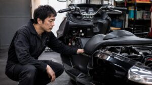 マグザムのような大型スクーターの電装系を確認する日本人メカニック